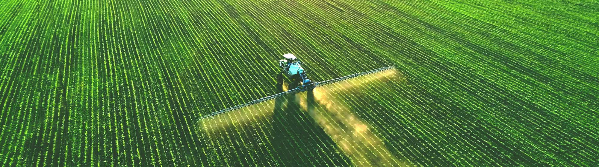 Une machine à épandage qui pulvérise un produit dans un champ vert. Le matériel agricole est intégré à SIA’PRO.